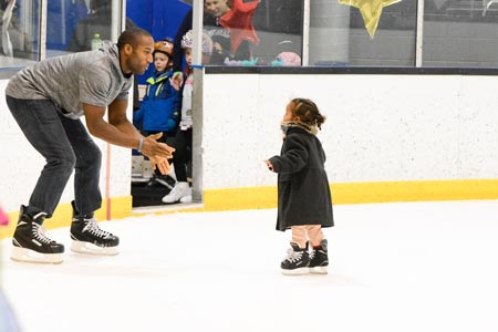 Little girl ice skating to her father.